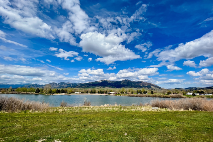 Scenic landscape with mountains, lake, grassy field, and clouds.