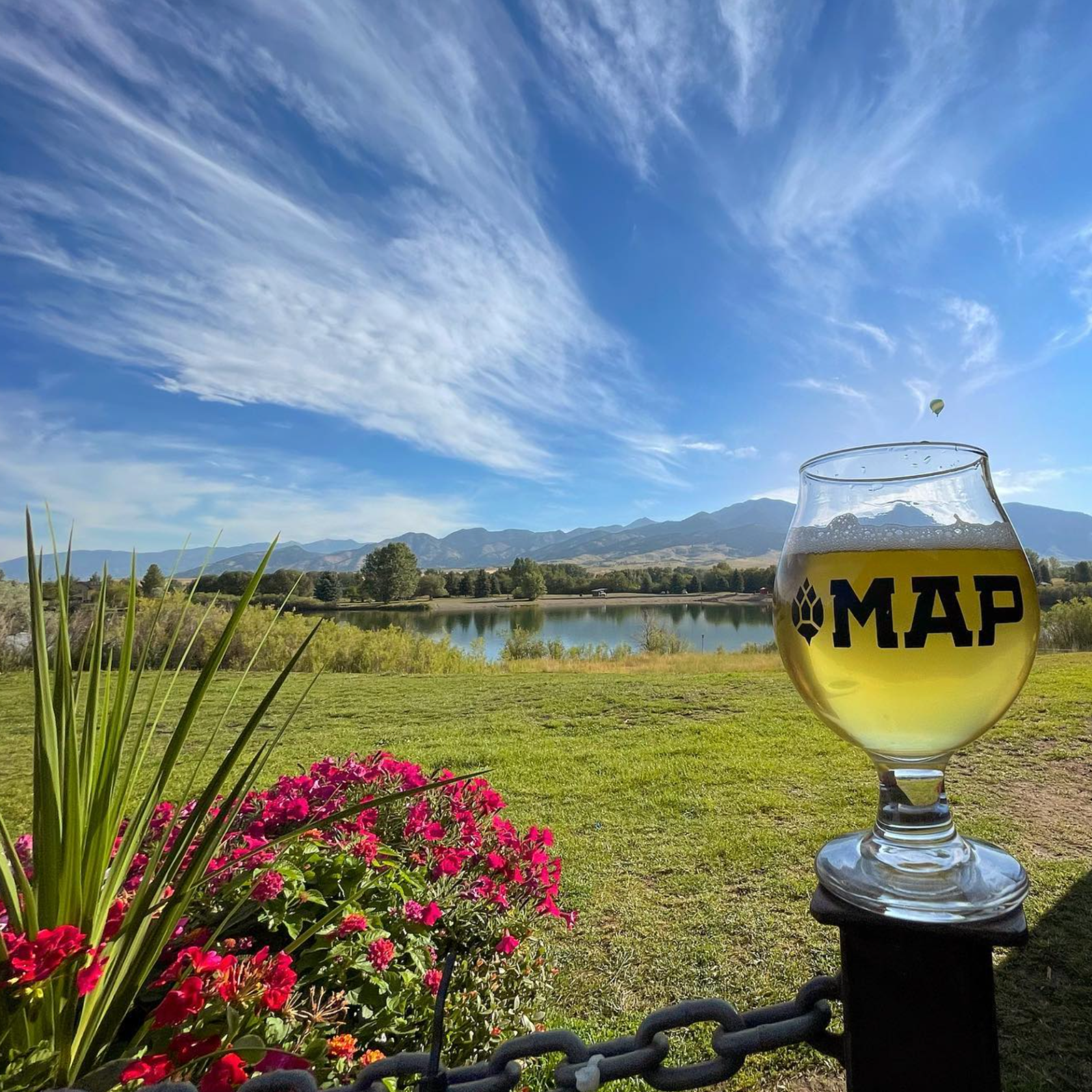 Beer glass on rail overlooking lake, mountains, and sky.