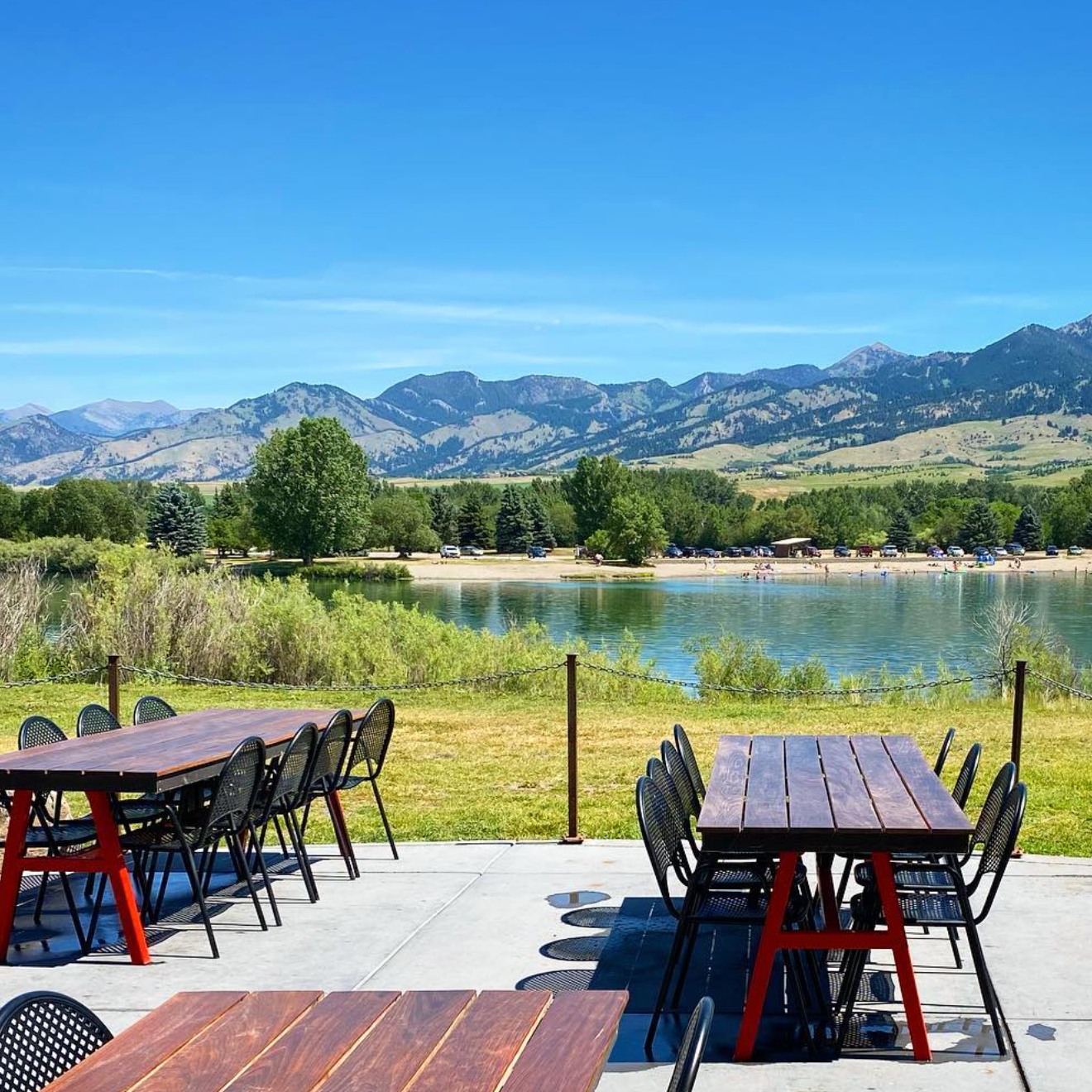 Outdoor seating with tables, mountain view, and lake under clear blue sky.