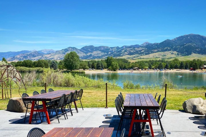 Outdoor seating with tables, mountain view, and lake under clear blue sky.