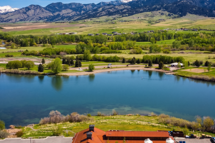 Aerial view of a lake with a building, fields, and mountains in the background.