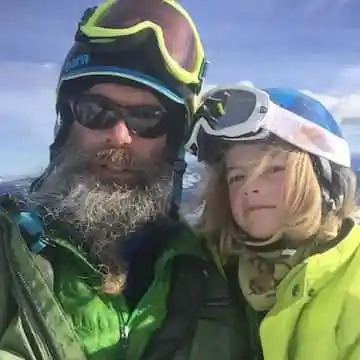 Two people in ski gear with snowy mountains in the background.