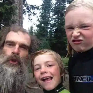 Bearded man with two smiling kids in forest setting.