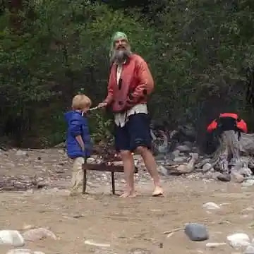 Man and child at a campsite in a forested area.