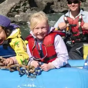 Group of people in life vests smiling on a rafting boat.